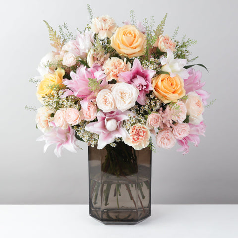 Bouquet of flowers in a clear vase on a white surface with a gray background